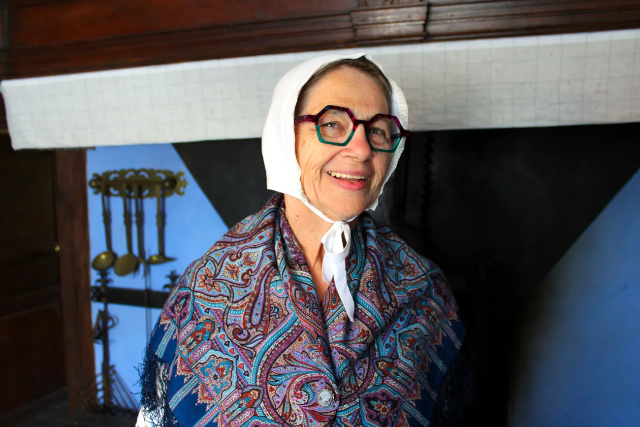 Membre active du Comité de La Blanche Maison, Annie Duterme est photographiée en costume traditionnel ardennais dans la cuisine de la Blanche Maison le 14 juin 2026 lors de l’inauguration de l’exposition dédiée à Saint Hubert. Ⓒ 2026 CC BY-NC 4.0 Gilles Pirlot de Corbion