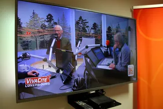 Dans la pièce qui jouxte le studio, un écran de télévision affiche en direct l’interview de Gilles Pirlot de Corbion à Luxembourg Matin