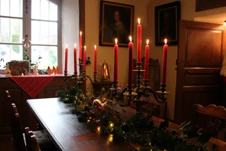 Sur la table de la belle salle de la Blanche Maison, décorée de branches de houx et de sapin, deux candélabres portent des bougies rouges allumées lors du goûter de Noël le 20 décembre 2025 à Nisramont.