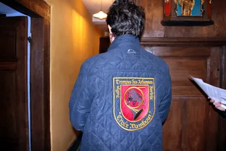 Signe des traditions cynégétiques en Ardenne belge et de la préservation de l’identité ardennaise, l’écusson de forme héraldique et richement brodé des sonneurs de la Croix Mambour à Bertrix représente un sanglier et une trompe de chasse avec des inscriptions en lettres dorées autour du blason.