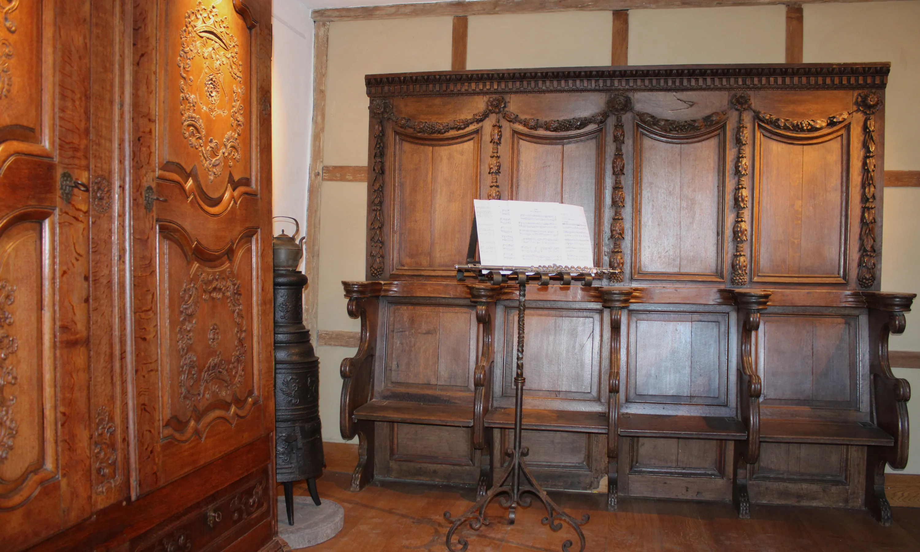 Au premier plan, une imposante garde robe aux portes sculptées sur lesquelles figurent notamment des couronnes héraldiques. Ce chef-d’œuvre de Nicolas Mathieu, menuisier à Vielsalm durant le troisième quart du XVIIIe siècle, est un exemple des plus belles productions ardennaises de l’époque. A l’arrière-plan, un ensemble de quatre stalles d’église surmontées d’une boiserie de style baroque avec ses guirlandes aux motifs végétaux. Ⓒ 2024 CC BY-NC 4.0 Gilles Pirlot de Corbion