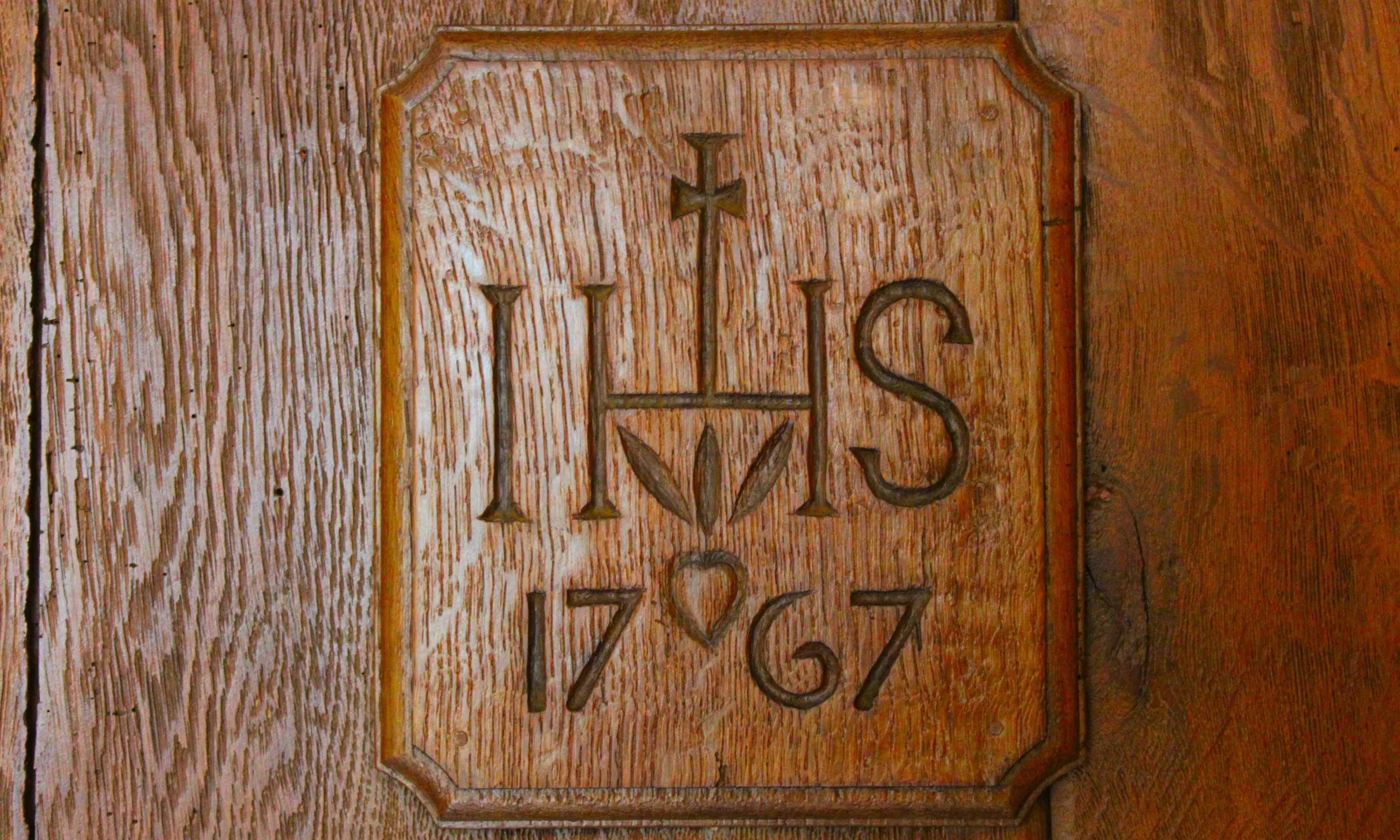 Plaquette de chêne foncé, créée en 2023 par Jacques Wanlin, portant la date d’achèvement de la Blanche Maison (1767). Les chiffres sont surmontés du trigramme IHS, correspondant à Iesus Hominum Salvator (Jésus Sauveur des Hommes), accompagné d’une croix et des trois clous de la Passion du Christ. Ⓒ 2024 CC BY-NC 4.0 Gilles Pirlot de Corbion