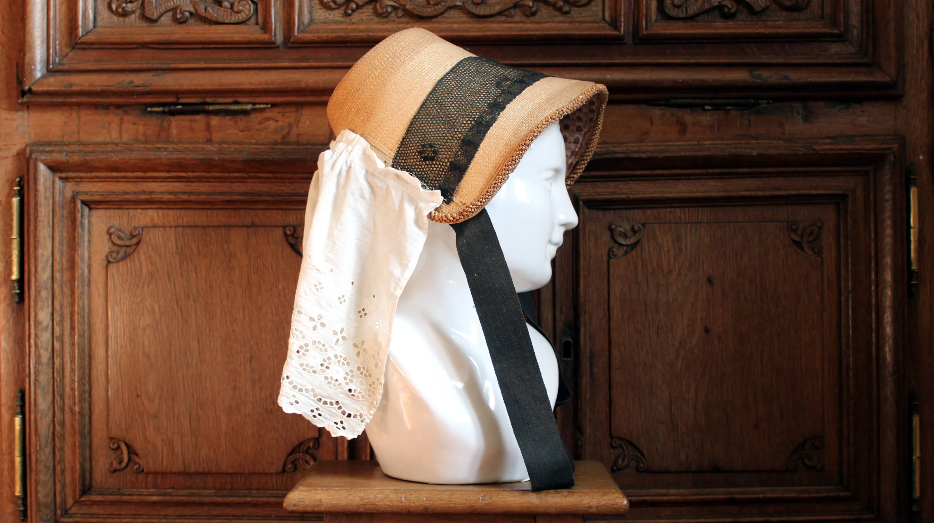 Devant un meuble en chêne sculpté aux motifs baroques créé par le maître-menuisier Jean-Georges Scholtus au début du XVIIIe siècle, buste en porcelaine blanche servant à présenter un barada, chapeau ardennais traditionnel, en paille, prolongé par un volant d'étoffe ou de dentelle pour protéger le cou du soleil. Ⓒ 2025 CC BY-NC 4.0 Gilles Pirlot de Corbion