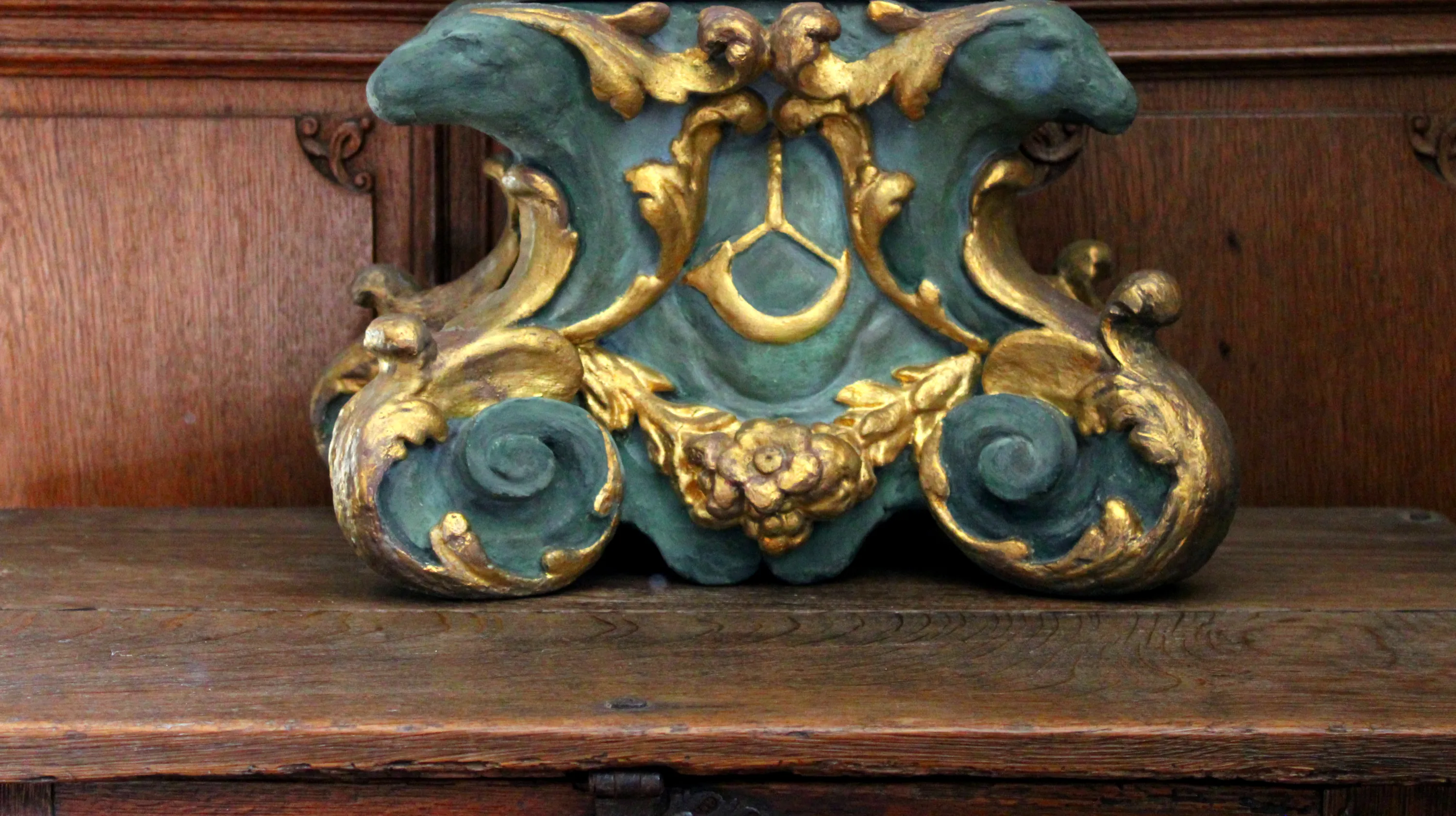 Ornement en bois sculpté avec des volutes symétriques, des guirlandes végétales, des rehauts dorés caractéristiques du style baroque et des têtes de cerfs stylisées encadrant un cor de chasse, motif emblématique des traditions cynégétiques en Ardenne belge Ⓒ 2025 CC BY-NC 4.0 Gilles Pirlot de Corbion