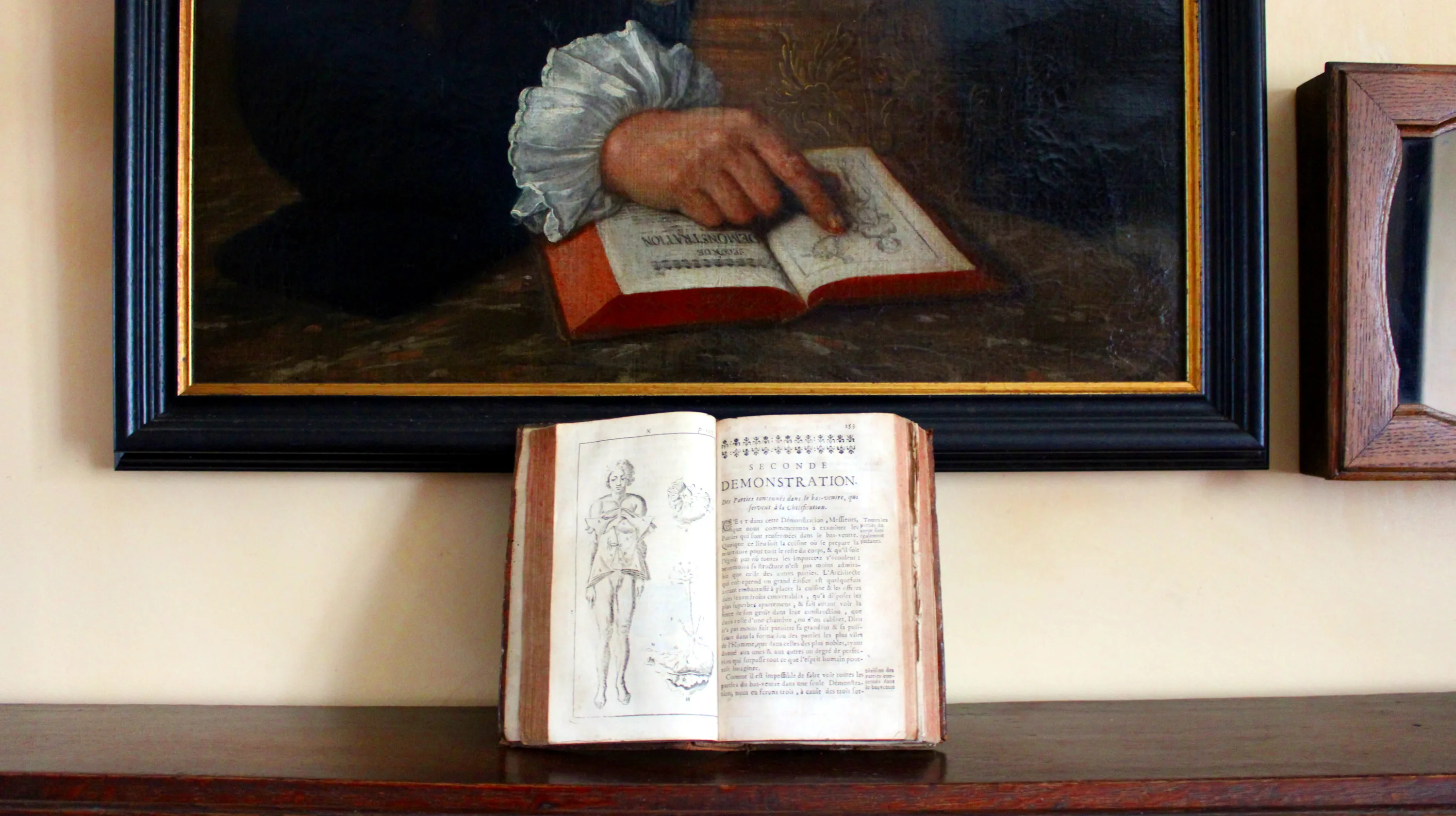 Ouvrage scientifique, rédigé à la fin XVIIe siècle par l’anatomiste français Pierre Dionis (1643-1718), exposé sur une commode-secrétaire devant un tableau peint par Louis-Félix Rhenasteine (1718-1799) représentant le chirurgien Erasme Gillard (1719-1776) qui pose la main droite, émergeant d’une manchette blanche, sur un exemplaire du même livre ouvert à la même page. Ⓒ 2026 CC BY-NC 4.0 Gilles Pirlot de Corbion