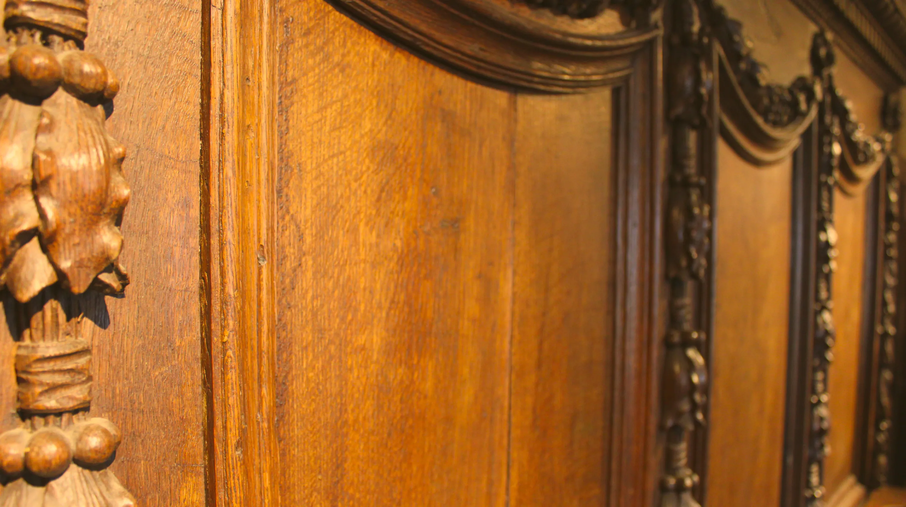 Quatre stalles en chêne sculpté provenant d’un chœur d’église de la principauté de Liège, exposées dans la salle Saint-Hubert, présentent un dossier à panneau central lisse encadré de montants à chapiteaux composites ornés de feuilles d’acanthe stylisées, de volutes ioniques et de trois sphères superposées, le tout surmonté d’une corniche architecturée à frise de guirlandes végétales et de draperies baroques se prolongeant sur les pilastres adjacents. Ⓒ 2026 CC BY-NC 4.0 Gilles Pirlot de Corbion