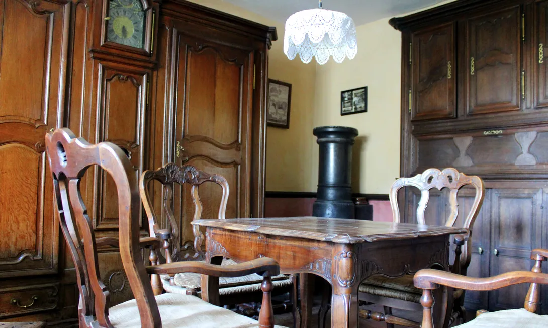 La grande armoire, où deux portes moulurées encadrent une gaine d’horloge, provient de l’ancien hôtel d’Orange à Stavelot. A sa droite se trouve un placard de taque, un aménagement typiquement ardennais. Au centre, une table et des fauteuils permettaient de passer ensemble les longues soirées d’hiver à côté du poêle. Ⓒ 2024 CC BY-NC 4.0 Gilles Pirlot de Corbion